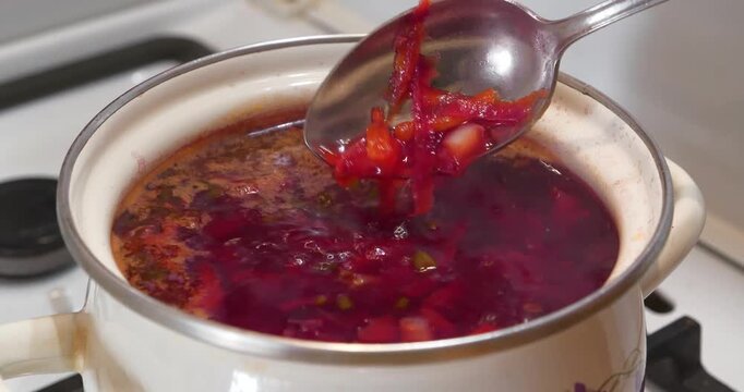 Ukrainian borscht is cooked on stove. National dish of Ukraine. Main first course of Ukrainian cuisine. Cook stirs borscht with spoon. Cooking first courses.Red Ukrainian borsch is boiling in saucepan