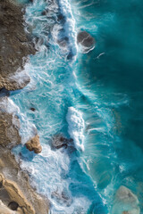 Fototapeta premium Waves crashing on rocky shore. Ocean view from above. Turquoise water meets earth in a dynamic display of coastal beauty.