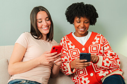 Two joyful females are engrossed in their smartphones, sharing delightful moments and experiences through various applications and social media, showcasing the bond of friendship and modern