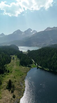 Aerial drone view of Lake Lej da Staz (Mej de Staz) surrounded by pine forest and mountains near St. Moritz in Engadin, Switzerland. Scenic alpine landscape with lakes, forests, and peaks. Perfect for