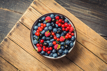 Freshly harvested berries in bowl on the rustic background. Summer berries. Shot from above.
