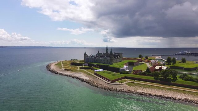 Aerial video of the coastal castle Kronborg with a dark cloud and vibrant water in the background.
