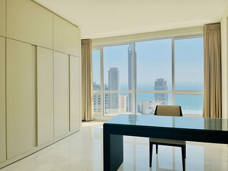 Modern apartment interior with large window overlooking a city skyline and ocean view from a dining table
