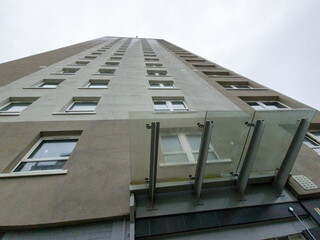 Fototapeta premium A modern building with a multi-window façade. The perspective is oblique, creating a sense of depth and height. The lower section of the building features a glass canopy for the entrance. 