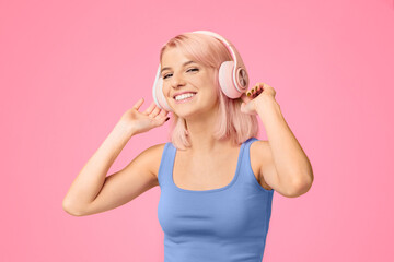 Carefree woman listening favorite music in wireless headphones on yellow studio background. Lovely...