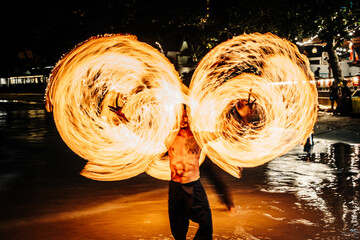 Fire dancer performing with flames at night on the beach