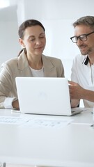 Businessman and adult businesswoman reviewing marketing analytics on laptops, working together strategically in contemporary workplace with minimalist interior design and collaborative atmosphere