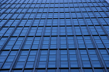 Obraz premium Modern skyscraper facade featuring a grid of reflective glass windows, showcasing architectural design and urban environment with a striking blue hue and geometric patterns