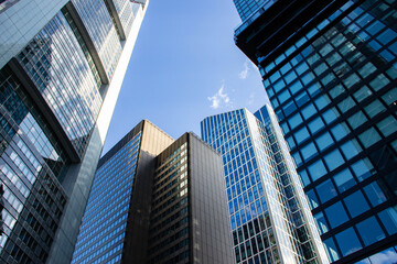 Modern skyscrapers with reflective glass facades rise against a clear blue sky, showcasing urban architecture and innovative design in a bustling city environment
