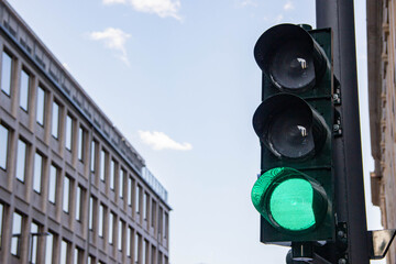 Green traffic light signaling go for vehicles, positioned on a street corner with modern buildings and blue sky in the background, representing urban transportation and safety