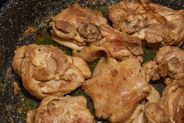 Pieces of chicken meat are fried in a frying pan, exuding flavor and mouth-watering appearance. Delicious chicken pieces are fried in a frying pan until golden brown.