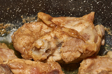 Pieces of chicken meat are fried in a frying pan, exuding flavor and mouth-watering appearance. Delicious chicken pieces are fried in a frying pan until golden brown.