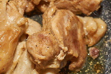 Pieces of chicken meat are fried in a frying pan, exuding flavor and mouth-watering appearance. Delicious chicken pieces are fried in a frying pan until golden brown.