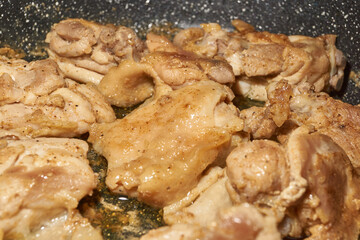 Pieces of chicken meat are fried in a frying pan, exuding flavor and mouth-watering appearance. Delicious chicken pieces are fried in a frying pan until golden brown.
