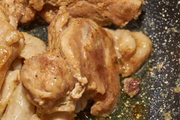 Pieces of chicken meat are fried in a frying pan, exuding flavor and mouth-watering appearance. Delicious chicken pieces are fried in a frying pan until golden brown.