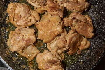 Pieces of chicken meat are fried in a frying pan, exuding flavor and mouth-watering appearance. Delicious chicken pieces are fried in a frying pan until golden brown.