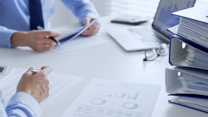 Accountants are analyzing financial reports with magnifying glass and documents, performing accounting and auditing tasks in the office, close up. Audit and taxes in business