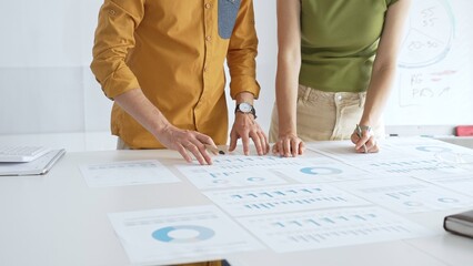 Business professionals analyzing financial reports, pointing at charts during collaborative meeting, discussing data with focused professional demeanor