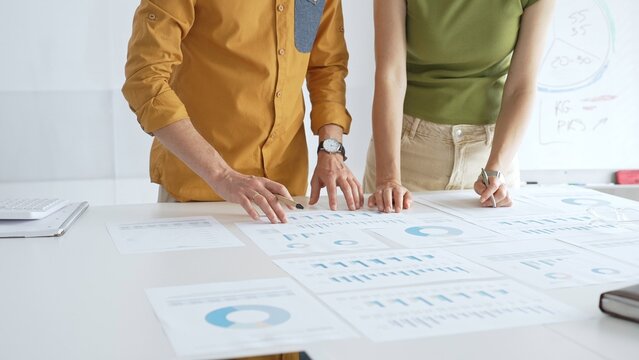 Business professionals analyzing financial reports, pointing at charts during collaborative meeting, discussing data with focused professional demeanor