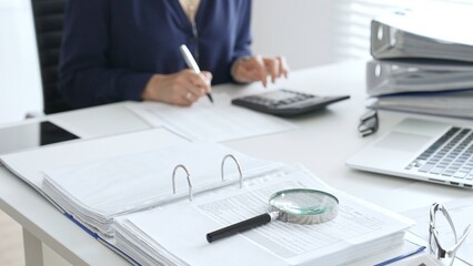 Professional analyzing financial data, writing notes near laptop, magnifying glass, documents,...