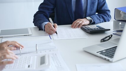 Close up of female accountant hands using calculator while collaborating with male colleague in...