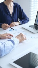 Businessman and businesswoman using laptop while looking through documents, pointing at charts and graphs during a meeting in bright office. Business people concept