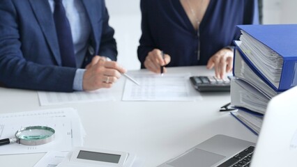 Magnifying glass and calculator over financial documents opposite financial team of male and female auditors, reviewing reports, collaborating on accounting details in office. Audit and taxes