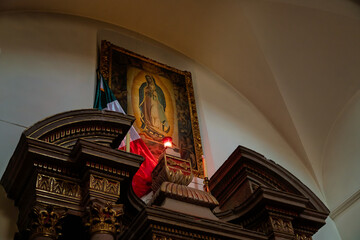 Framed image of Our Lady of Guadalupe with Mexican flag and red light inside colonial church
