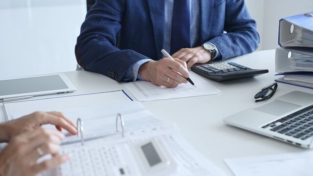 Close up of female accountant hands using calculator while collaborating with male colleague in office, calculating taxes and analyzing financial data. Audit and taxes in business