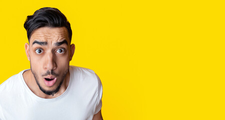 Closeup portrait of amazed bearded arab man looking at camera over yellow studio background, copy...