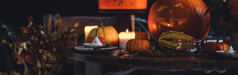 Beautiful table with homemade delicious cake for Halloween party with meringue ghosts and chocolate pumpkins. Candles in chandelier, spider web, jack-o-lantern for festive holiday decoration. Banner