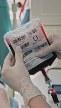 Vertical close-up shot of unrecognizable nurse, wearing gloves, examining blood bag after donation in clinic