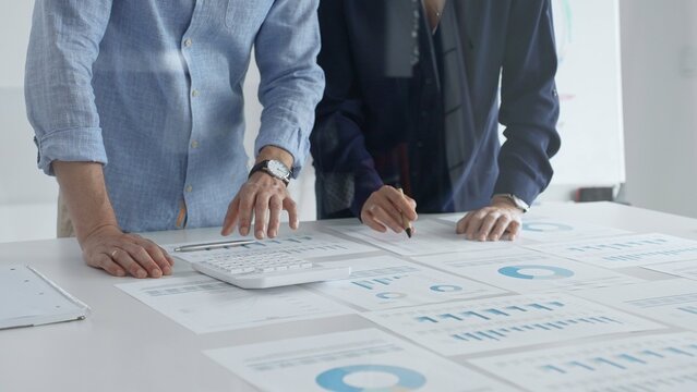 Business professionals analyzing financial charts, gesturing over spreadsheets during collaborative meeting in contemporary workspace, discussing data driven insights