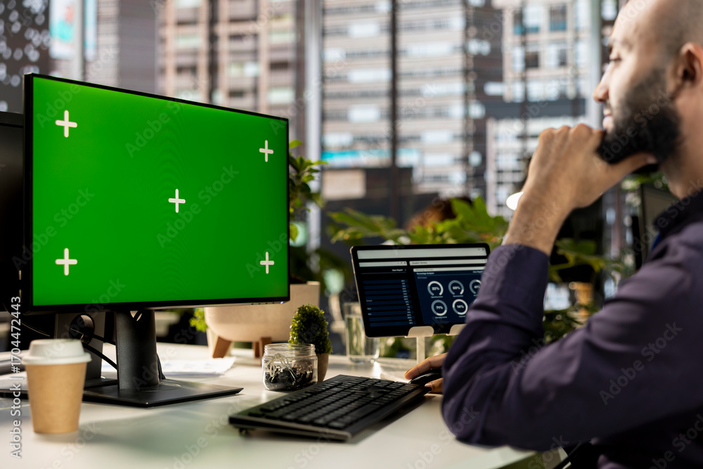 Poster middle eastern man working on accounting tasks next to green screen on pc, evaluating online analyti