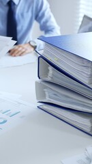 Corporate professionals reviewing financial documents, working collaboratively at white desk with blue folder stack, highlighting teamwork and business productivity. Audit and taxes in business