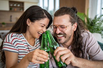 Happy couple laughing and toasting with beer bottles at home