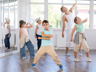 Naklejka premium In sports studio, creative childrens team learns hip-hop dance accompanied by experienced man teacher