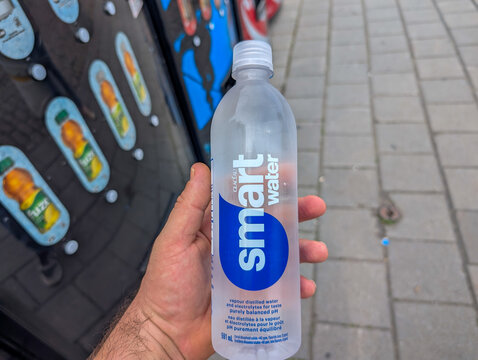 Canada, 05 July 2025 : Hand holding smart water bottle beside vending machine on city sidewalk