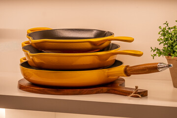 Stack of vibrant yellow frying pans with black interiors resting on wooden cutting board, showcasing kitchen cookware and modern culinary design elements in a cozy kitchen setting