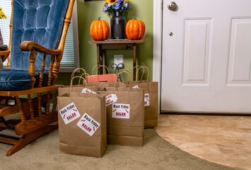 Several brown paper bags are strategically placed at the entrance, showcasing Black Friday sales. The cozy entryway features pumpkins, a rocking chair, and seasonal decorations.