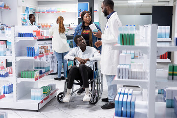 Obraz premium African American medical staff advising a customer with disability about prescription drugs use or medication dosage, pharmaceutical service during a pharmacy retail visit focused on health.