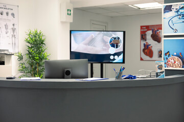 Unoccupied front desk in clinic lobby, organized with supplies and flyers. Clean, modern hospital...