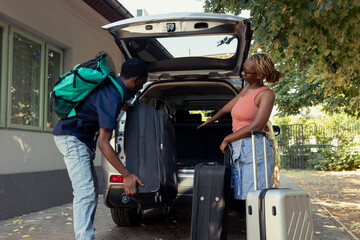 With luggage in hand and hearts full of joy, cheerful couple loads their car for a holiday ride. Young people in love preparing for a weekend road trip together, exploration and adventures.
