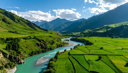 Scenic aerial view of a turquoise river snaking through vibrant green farmlands, surrounded by majestic, snow-capped mountains