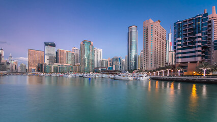 Obraz premium Dubai Marina towers and yachts reflected in water of canal in Dubai day to night timelapse