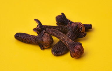 Close-up of dried cloves on a bright yellow background. Aromatic spice used in cooking, baking and traditional remedies. Strong scent, rich flavor and natural herbal ingredient.