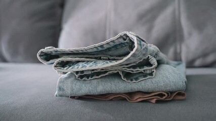 Close up of person carefully placing folded jeans on brown cloth stacked on couch showing detail of fabric care domestic household task organization lifestyle clothing maintenance