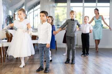 Elegantly dressed children, preteen girls and boys performing curtsy and bow during festive dance event at school, showcasing traditional gesture of etiquette