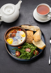 Baked eggs with vegetables in clay bowl, served with ciabatta bread and fresh salad