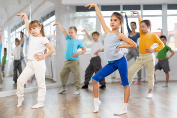 Fototapeta premium Children studying modern style dances with female teacher in dance class indoors